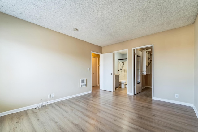 empty room featuring heating unit, a textured ceiling, baseboards, and wood finished floors