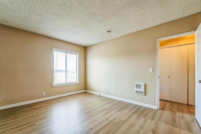 empty room with baseboards, a textured ceiling, heating unit, and wood finished floors