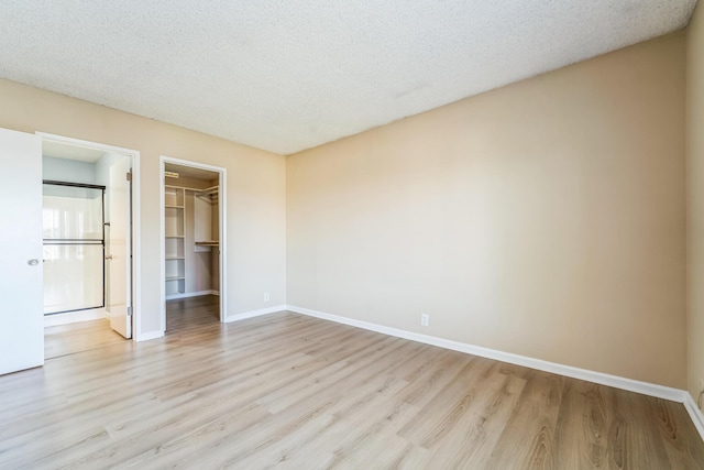 unfurnished bedroom featuring a spacious closet, a textured ceiling, baseboards, and wood finished floors