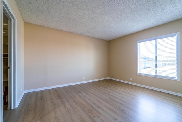 empty room featuring a textured ceiling, wood finished floors, and baseboards