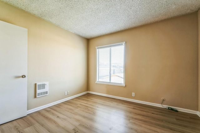 spare room with a textured ceiling, baseboards, wood finished floors, and heating unit