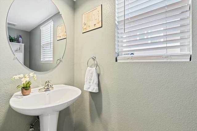 bathroom featuring plenty of natural light, a textured wall, visible vents, and a sink