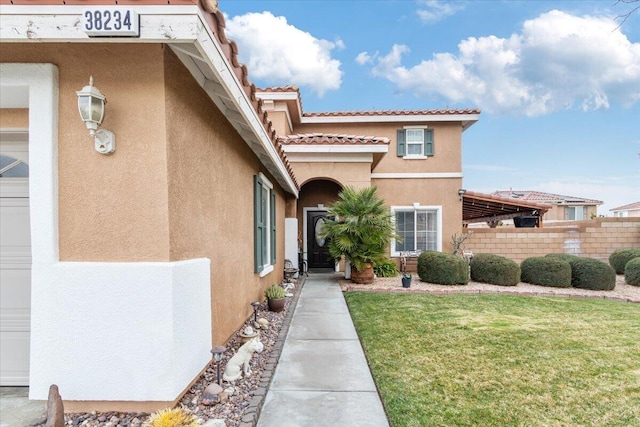 property entrance with stucco siding, a yard, and fence