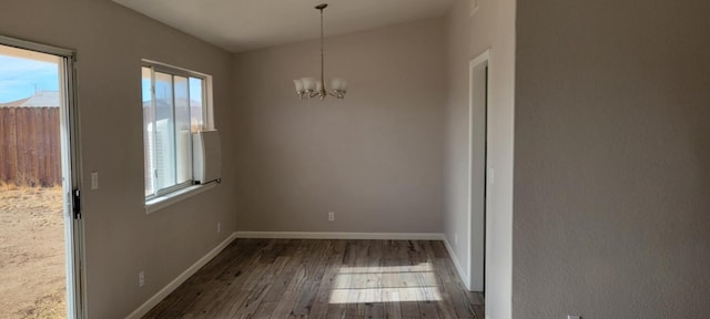 unfurnished dining area with a wealth of natural light, dark hardwood / wood-style floors, and an inviting chandelier