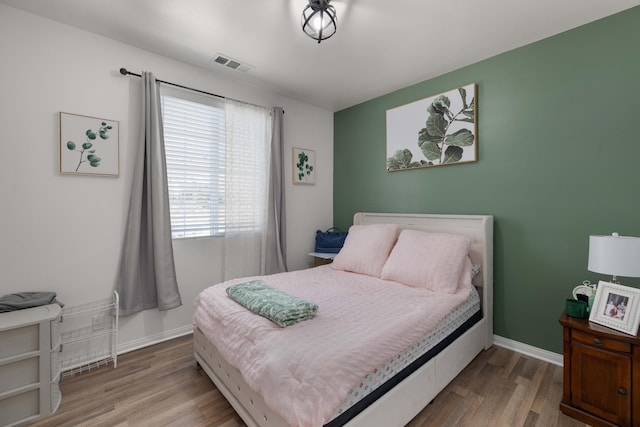 bedroom with visible vents, wood finished floors, and baseboards