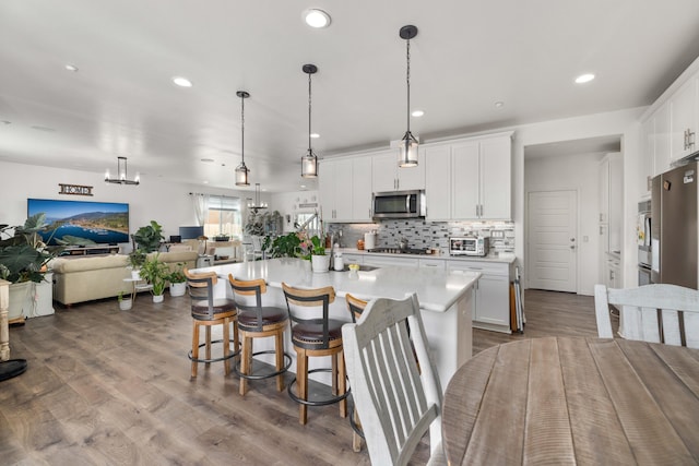 kitchen featuring open floor plan, white cabinetry, backsplash, light countertops, and appliances with stainless steel finishes