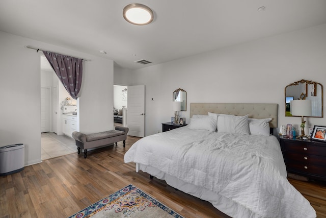 bedroom featuring connected bathroom, visible vents, and wood finished floors