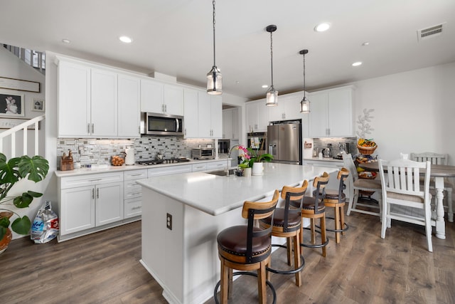 kitchen featuring a sink, stainless steel appliances, an island with sink, decorative backsplash, and light countertops