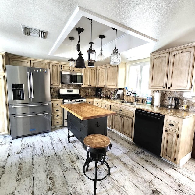 kitchen featuring wood counters, stainless steel appliances, a raised ceiling, sink, and a center island