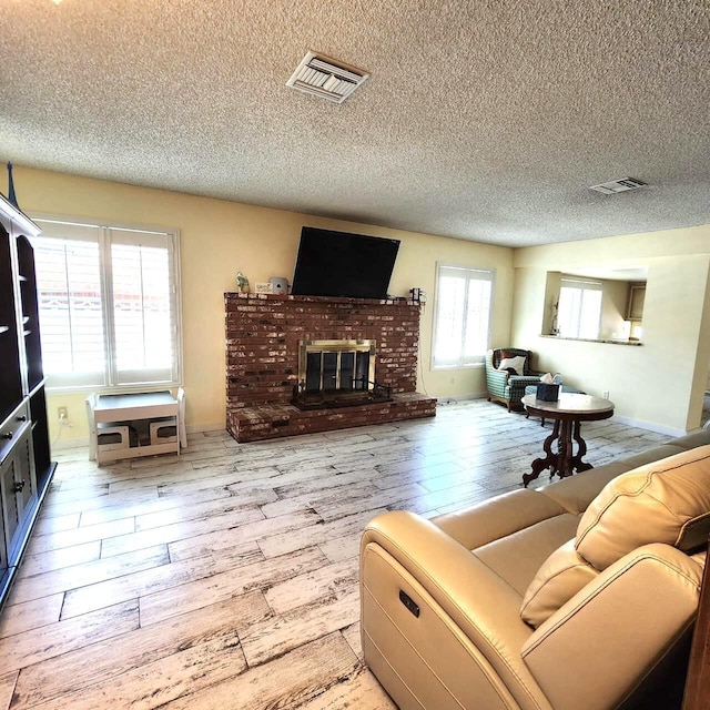 living room featuring a fireplace, a textured ceiling, light hardwood / wood-style floors, and plenty of natural light