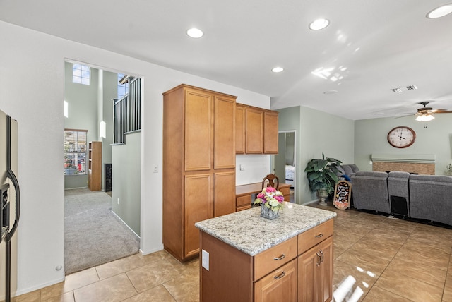 kitchen featuring ceiling fan, a kitchen island, light colored carpet, and light stone counters