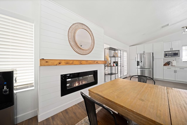 dining room featuring wood finished floors, a healthy amount of sunlight, a glass covered fireplace, visible vents, and lofted ceiling