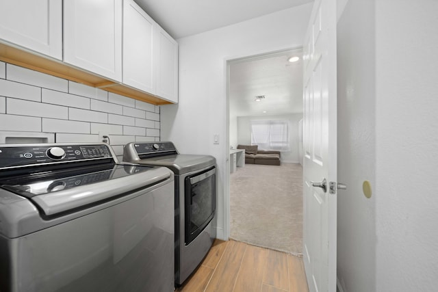laundry room featuring light wood-style flooring, washer and clothes dryer, and cabinet space