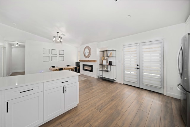 kitchen with a glass covered fireplace, vaulted ceiling, baseboards, white cabinets, and freestanding refrigerator