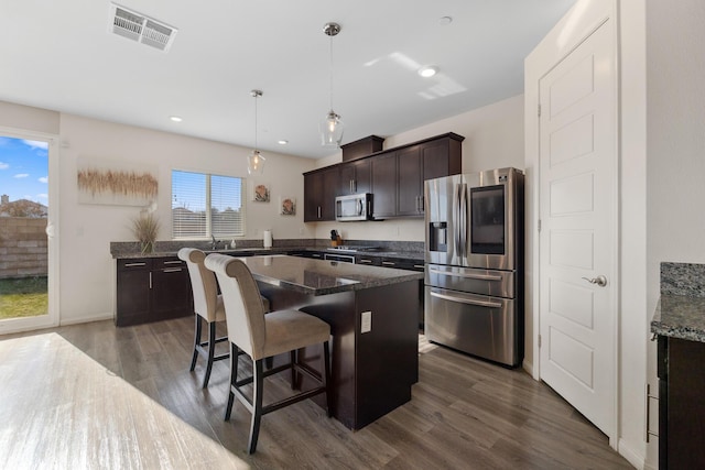 kitchen with dark brown cabinetry, hanging light fixtures, dark hardwood / wood-style flooring, dark stone counters, and appliances with stainless steel finishes