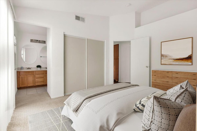 bedroom with vaulted ceiling, sink, light carpet, ensuite bath, and a closet