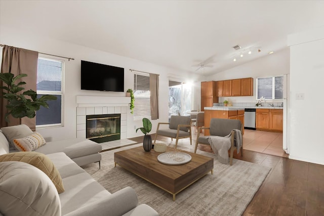 living room featuring sink, light hardwood / wood-style flooring, a tile fireplace, ceiling fan, and vaulted ceiling