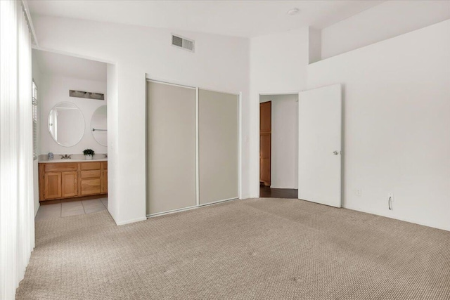 unfurnished bedroom with sink, light colored carpet, a closet, and ensuite bathroom