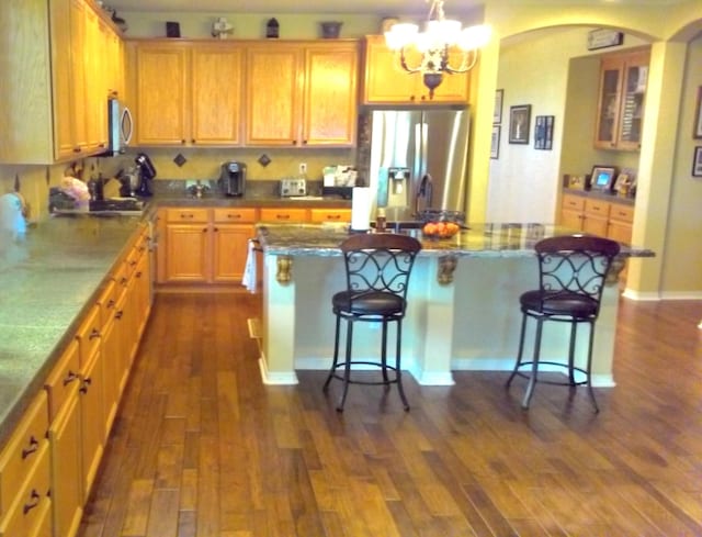 kitchen with a kitchen island, appliances with stainless steel finishes, dark hardwood / wood-style floors, and a kitchen bar