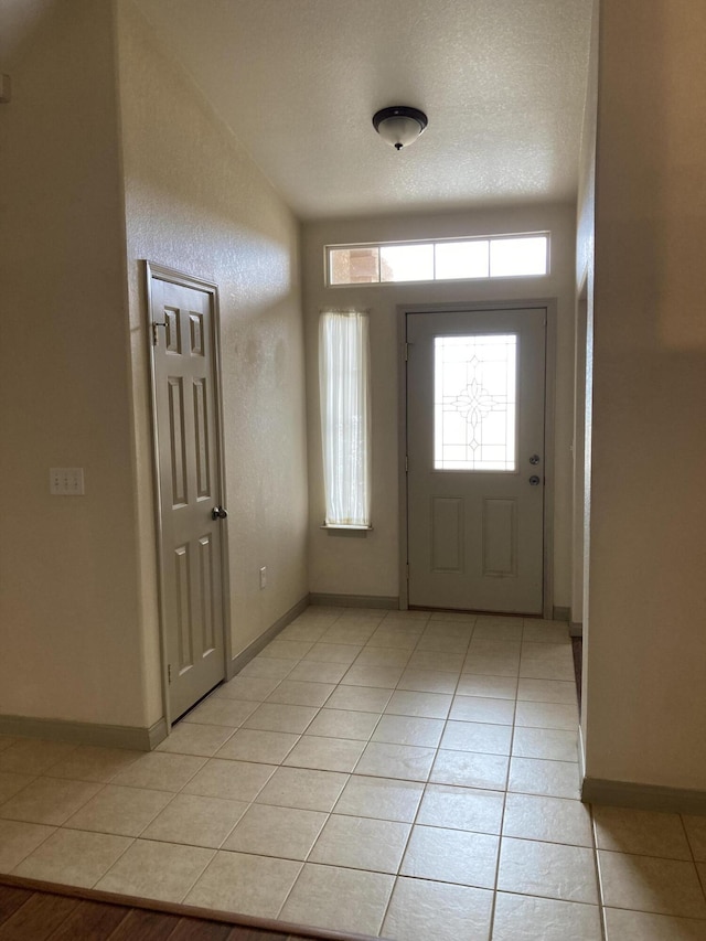 foyer featuring light tile patterned floors, baseboards, and a textured ceiling