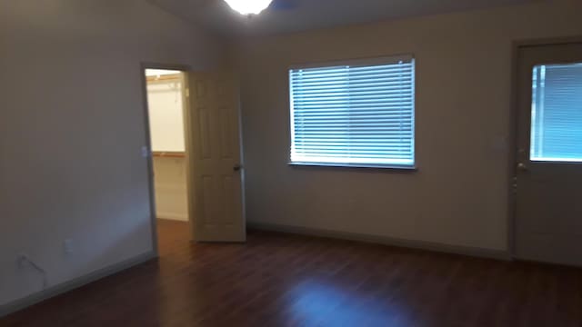 spare room featuring lofted ceiling, dark wood-style floors, and baseboards