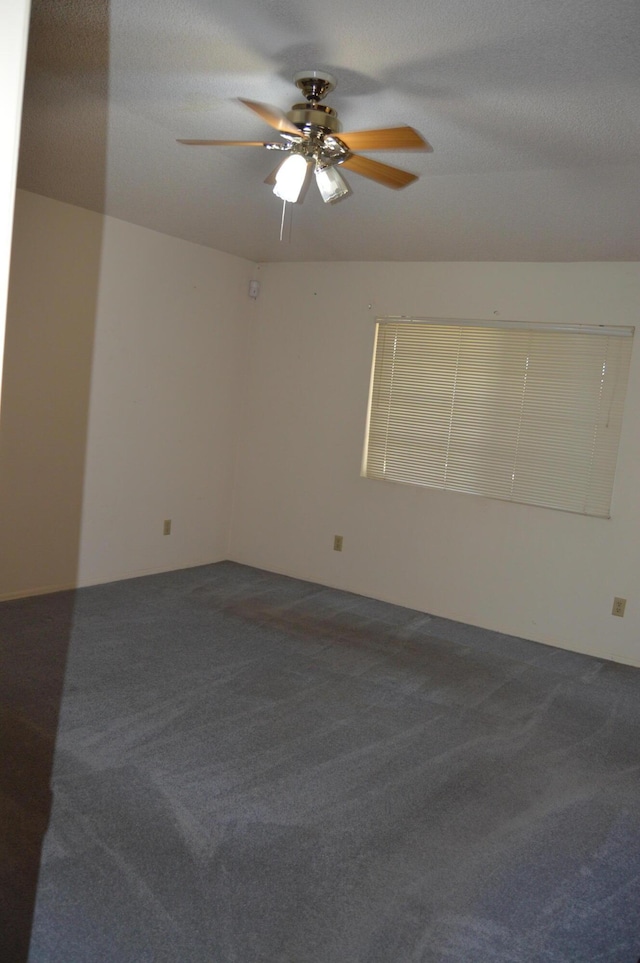empty room with a textured ceiling, dark carpet, and a ceiling fan