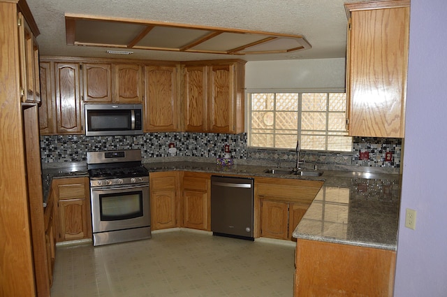 kitchen with a sink, backsplash, light floors, appliances with stainless steel finishes, and brown cabinetry