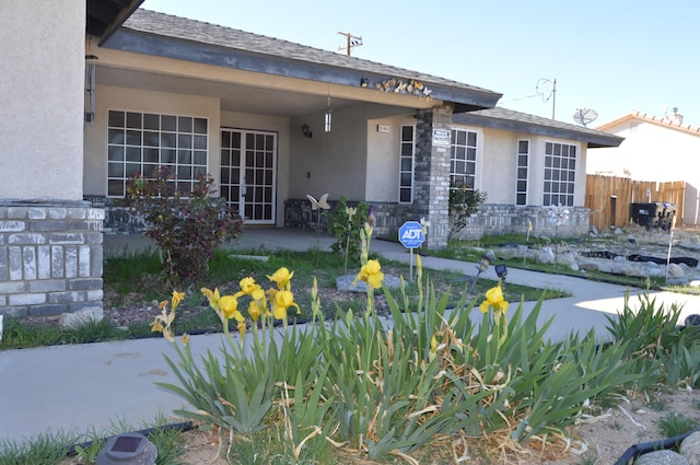 rear view of house featuring stucco siding, stone siding, and fence