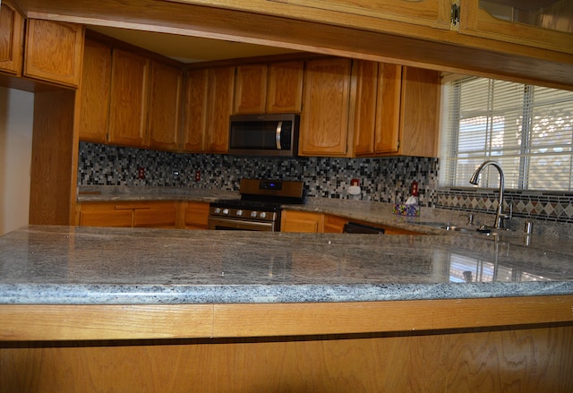 kitchen with stainless steel appliances, decorative backsplash, a sink, light stone countertops, and brown cabinetry