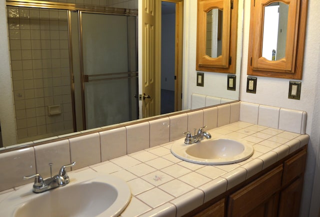 bathroom featuring a shower with door, double vanity, a sink, and backsplash