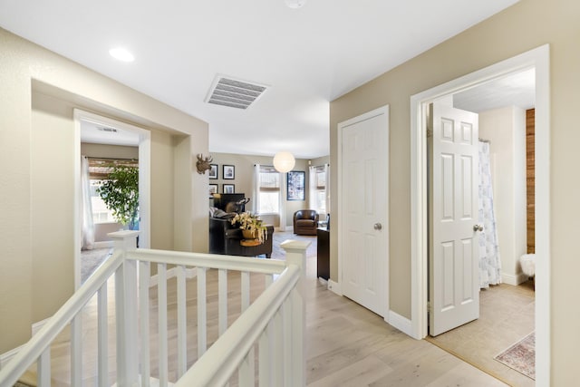 corridor featuring light wood finished floors, an upstairs landing, visible vents, and baseboards