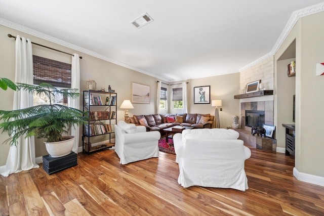 living area featuring a tile fireplace, wood finished floors, visible vents, and crown molding