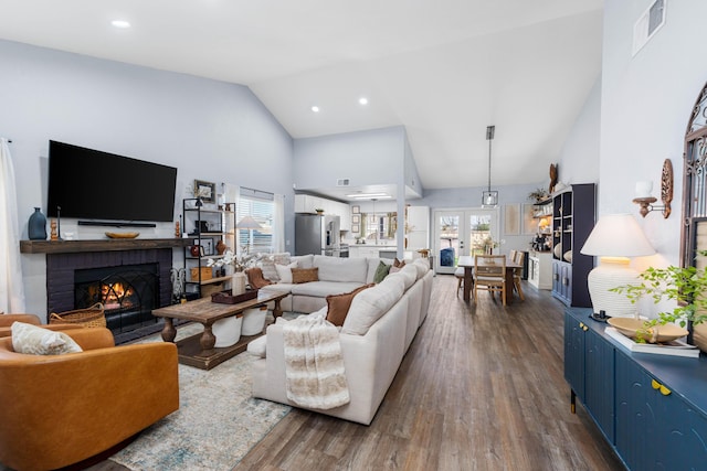 living area featuring french doors, dark wood-style flooring, visible vents, a brick fireplace, and high vaulted ceiling