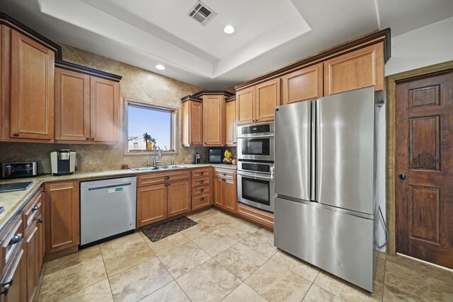 kitchen featuring sink, stainless steel appliances, a tray ceiling, decorative backsplash, and light tile patterned flooring