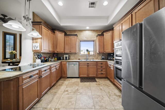 kitchen featuring sink, tasteful backsplash, pendant lighting, a tray ceiling, and appliances with stainless steel finishes