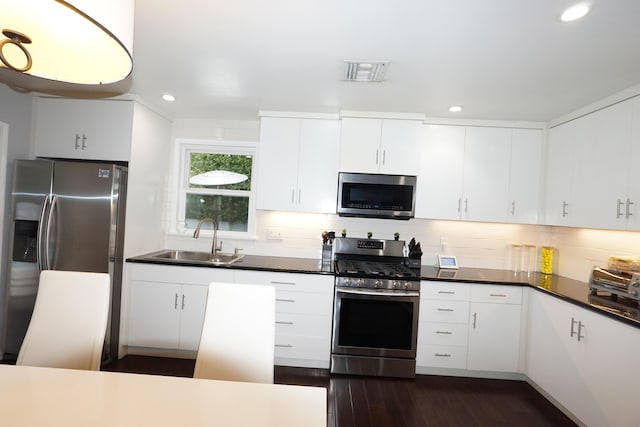 kitchen with stainless steel appliances, dark wood-style flooring, a sink, visible vents, and backsplash