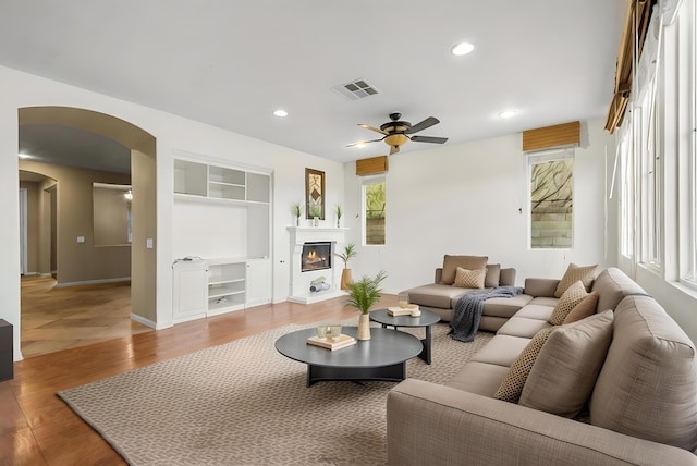 living room with visible vents, arched walkways, a glass covered fireplace, wood finished floors, and recessed lighting