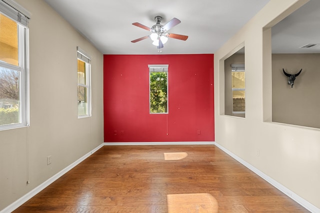 empty room with baseboards, visible vents, ceiling fan, and wood finished floors