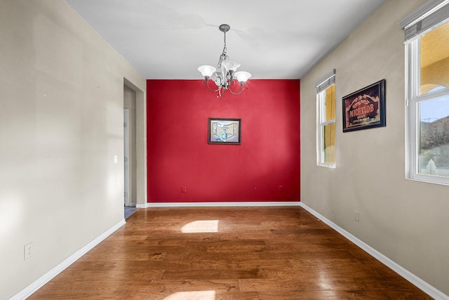 unfurnished dining area with an accent wall, baseboards, a chandelier, and wood finished floors