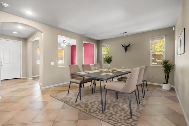 dining room with arched walkways, a healthy amount of sunlight, baseboards, and light tile patterned flooring