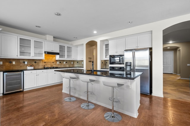 kitchen featuring arched walkways, appliances with stainless steel finishes, white cabinets, beverage cooler, and a kitchen breakfast bar