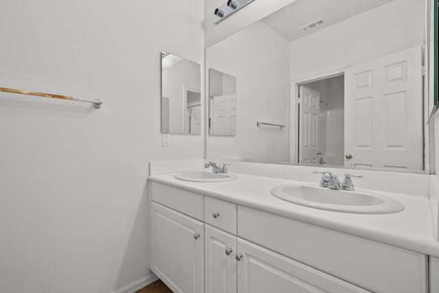 bathroom featuring double vanity, a sink, visible vents, and baseboards