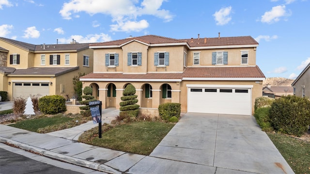 mediterranean / spanish-style home with a garage, concrete driveway, a tile roof, and stucco siding