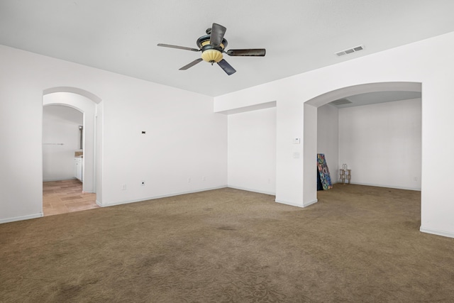 empty room featuring arched walkways, ceiling fan, light carpet, visible vents, and baseboards