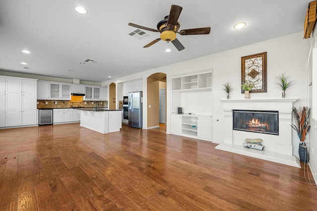 unfurnished living room featuring arched walkways, wine cooler, dark wood-style flooring, visible vents, and a glass covered fireplace