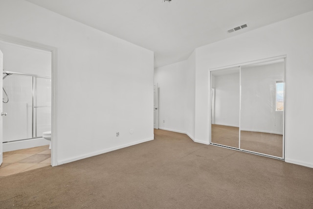 unfurnished bedroom featuring ensuite bathroom, a closet, carpet, and visible vents