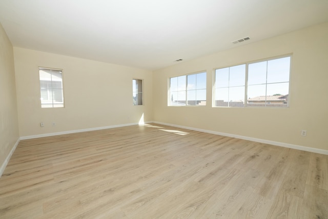 empty room with light wood-style flooring, visible vents, and baseboards