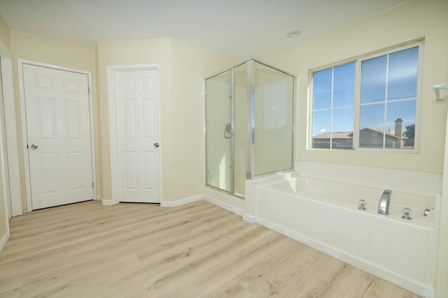 bathroom with a stall shower, baseboards, a bath, and wood finished floors