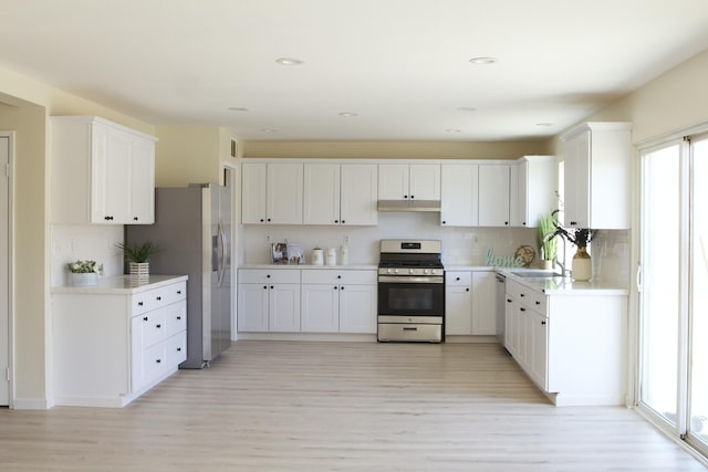 kitchen with light wood finished floors, stainless steel appliances, light countertops, white cabinetry, and a sink