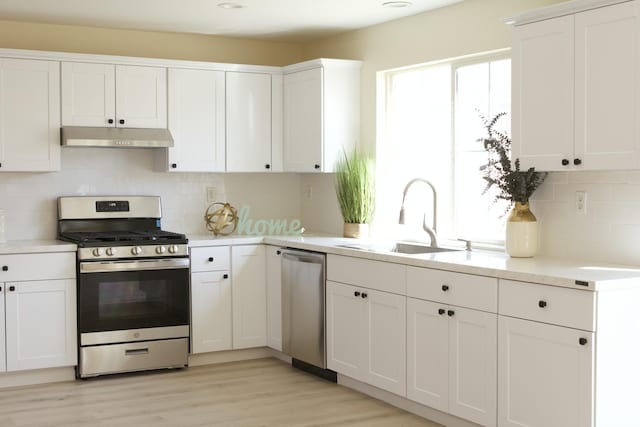 kitchen featuring under cabinet range hood, a sink, white cabinetry, light countertops, and appliances with stainless steel finishes